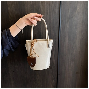 Detail of cream-colored bucket bag featuring a thin handle and brown leather pendant charm