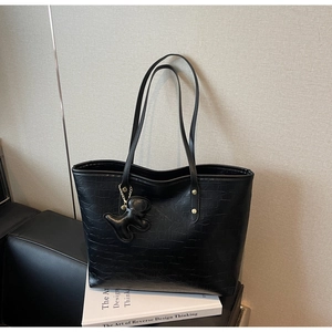 Detail of black faux leather tote with crocodile texture and dog-shaped charm