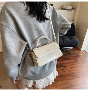 Detail of cream rectangular handbag with gold Fashion & Bags logo and slim shoulder strap