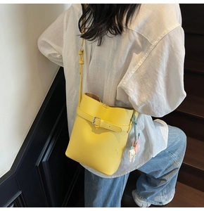 Detail of yellow lychee leather bucket bag with silver buckle strap and colorful charm