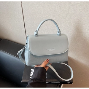 Detail of light blue textured leather handbag with embossed fashion logo and top handle
