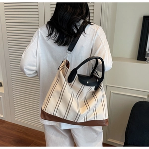 Detail of striped canvas tote bag showing embossed leather base and handle attachment