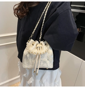 Detail of white lace bucket bag with pearl handle and golden chain strap for women