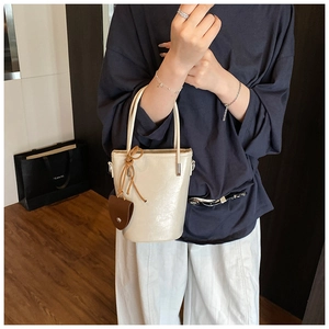 Detail of a creamy white glossy bucket bag featuring brown drawstring charm and thin straps