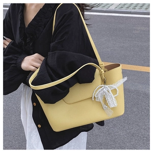 Detail of yellow tote bag featuring a pearl bow charm and litchi texture leather