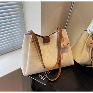 Detail of white crocodile pattern tote bag with brown leather straps and plush bear charm
