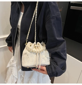 Detail of white bucket bag featuring floral embroidery and large faux pearl top handle