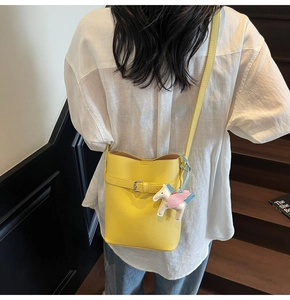 Detail of bright yellow lychee texture bucket bag worn on shoulder with unicorn charm
