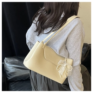Close-up of beige lychee texture tote bag with pearl lace bow charm on model shoulder