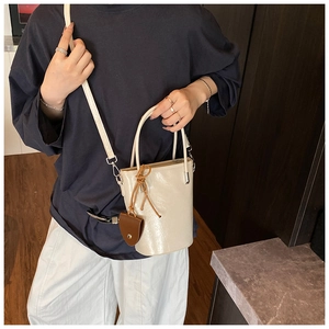 Close-up of a cream leather bucket bag with a brown charm and slender shoulder strap