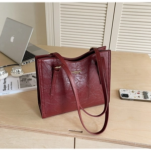 Detail of burgundy tote bag with pleated leather texture and gold lettering on desk