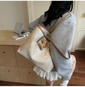 Detail of cream faux crocodile tote bag with brown handles and a puppy-shaped charm