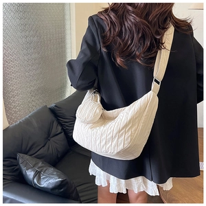 Detail of beige quilted half-moon crossbody bag with detachable round coin purse on shoulder