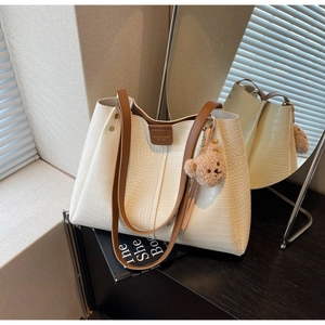 Detail of white crocodile embossed tote bag with brown straps and cute plush bear charm