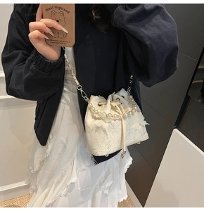 Detail view of white lace bucket bag with pearl handle and golden chain shoulder strap