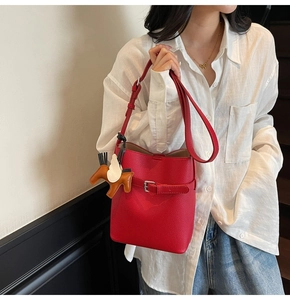 Detail of red lychee pattern bucket bag featuring a horse charm and adjustable strap