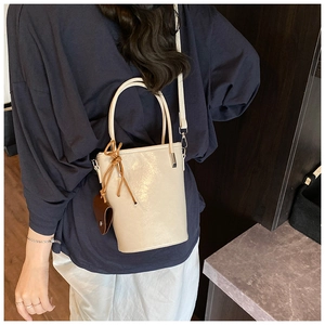 Detail view of cream bucket bag with round top handle and brown leather tassel charm