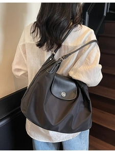 Minimalist black nylon tote bag with leather flap and metallic buckle worn on shoulder