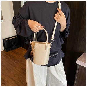 Detail view of cream bucket bag with smooth handles and detachable crossbody strap