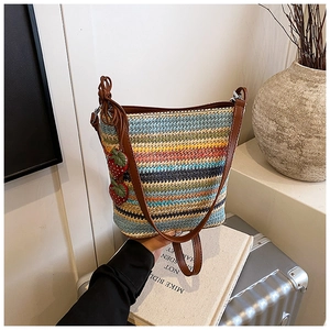 Detail of colorful woven bucket bag with leather strap and strawberry charms on a suitcase