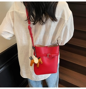 Detail of red lychee grain bucket bag featuring a winged horse charm on long shoulder strap