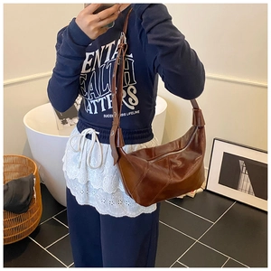 Détail d'un sac demi-lune marron foncé brillant avec une forme lisse et une large bandoulière