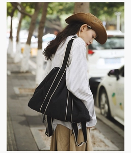 Close-up of black drawstring tote bag with contrast cream straps in outdoor street setting