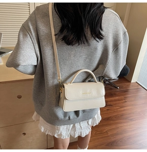 Close-up of a stylish cream PU leather small square bag with elegant gold lettering