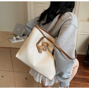 Detail of cream tote bag with crocodile embossed texture and a cute dog charm accessory