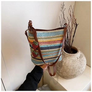 Detail of colorful rainbow striped woven straw bag with red strawberry charms and brown straps