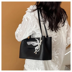 Detail of black tote bag featuring delicate white lace bow and pearl heart charm