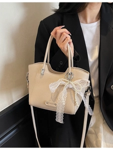 Sac cabas beige en cuir texturé avec nœud en dentelle porté par un mannequin