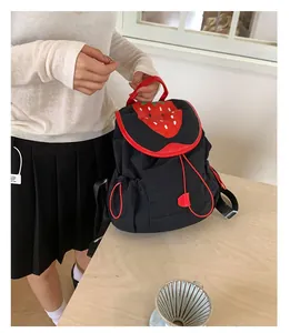 Macro view of a cute black mini backpack featuring a red strawberry lid on a wooden table