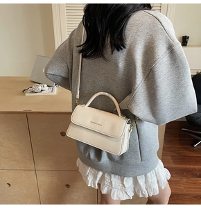 Detail view of cream leather crossbody bag with top handle and fashion logo lettering