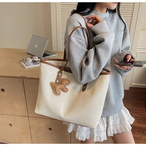 Detail of crocodile-embossed tote bag with brown trim and puppy-shaped leather charm