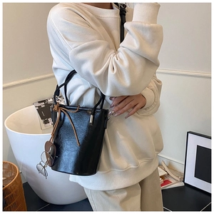 Detail of a black shiny leather bucket bag with a brown bow and retro glasses accessory