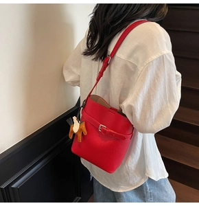 Detail of red lychee grain leather bucket bag featuring a decorative horse charm