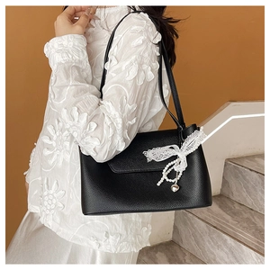 Detail of black lychee grain leather bag with white lace bow and pearl heart pendant
