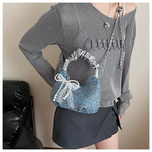 Detail of denim handbag with silver pleated handle, lace bow, and pearl charm