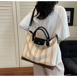 Close-up of striped canvas tote bag featuring black leather handles and flap closure