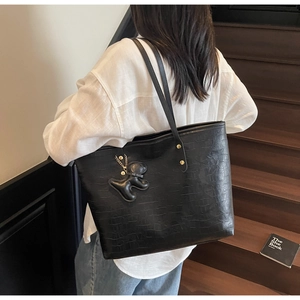 Detail of black faux crocodile leather tote bag featuring a cute bear keychain charm