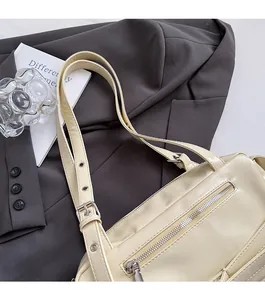 Close-up of cream leather shoulder bag with adjustable silver buckle straps on a grey blazer