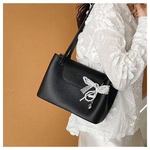 Detail view of black litchi leather tote bag with lace bow and pearl heart pendant decoration