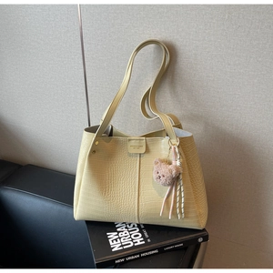 Detail of light beige tote bag with crocodile pattern and a cute bear keychain accessory