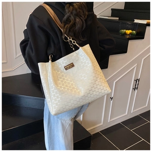 Sac fourre-tout crème chic avec logo embossé et bandoulière chaîne sur un mannequin moderne