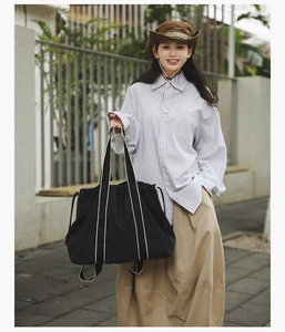Detailed view of black drawstring tote bag with striped straps in an outdoor casual setting