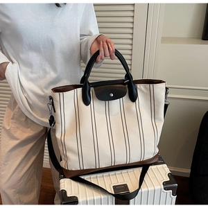 Detailed view of the striped canvas tote bag with leather flap and handles on a suitcase