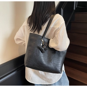Detail of black faux crocodile leather tote bag with small bear charm accessory