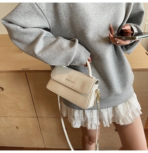 Detail showing cream white square handbag with golden hardware and adjustable strap