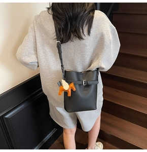Detail of black lychee grain leather bucket bag with orange pony charm on grey casual outfit